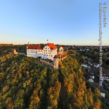 Burg auf bewaldetem Hügel mit umliegender Stadt bei klarem Himmel im Abendlicht
