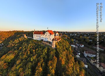 Burg auf bewaldetem Hügel mit umliegender Stadt bei klarem Himmel im Abendlicht