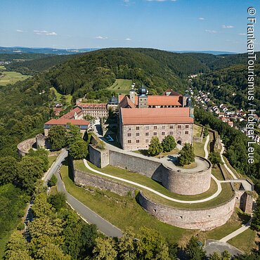 Die Luftaufnahme einer Burg auf einem zum Teil bewaldeten Hügel